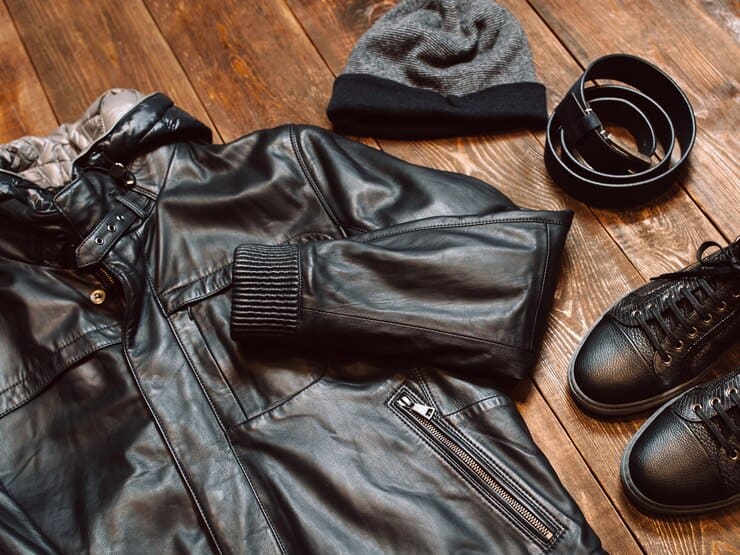 A stylish arrangement of vegan leather jacket, hat, shoes, and gloves displayed on a wooden floor, showcasing 2025 fashion trends.