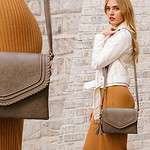 A stylish brown crossbody bag with decorative stitching and a tassel detail, worn by a woman dressed in a ribbed camel-colored skirt and a white jacket. The image is split into two sections, one showing a close-up of the bag and the other displaying the full outfit as the woman poses against a textured brick wall.