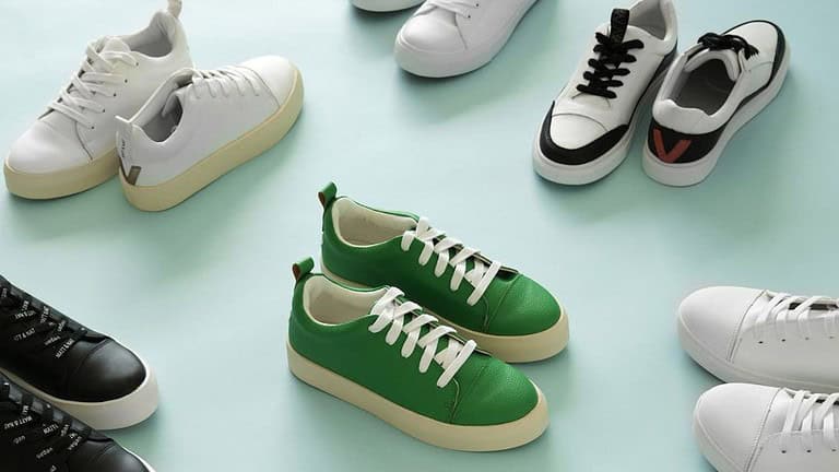 A collection of stylish sneakers displayed on a light blue background. The sneakers include a variety of designs and colors, with a prominent green pair with white laces in the center. Other sneakers in the image include white, black, and combinations of white with black or colored accents, arranged in a scattered yet aesthetically pleasing manner.