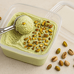 Vegan pistachio ice cream in a plastic container with a scoop on top, garnished with chopped pistachios and surrounded by scattered nuts on a beige surface