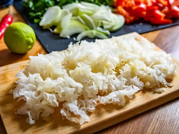 Freshly cut snow fungus (Tremella fuciformis) on a wooden cutting board with chopped vegetables in the background, highlighting its translucent, jelly-like texture for cooking and skin benefits.