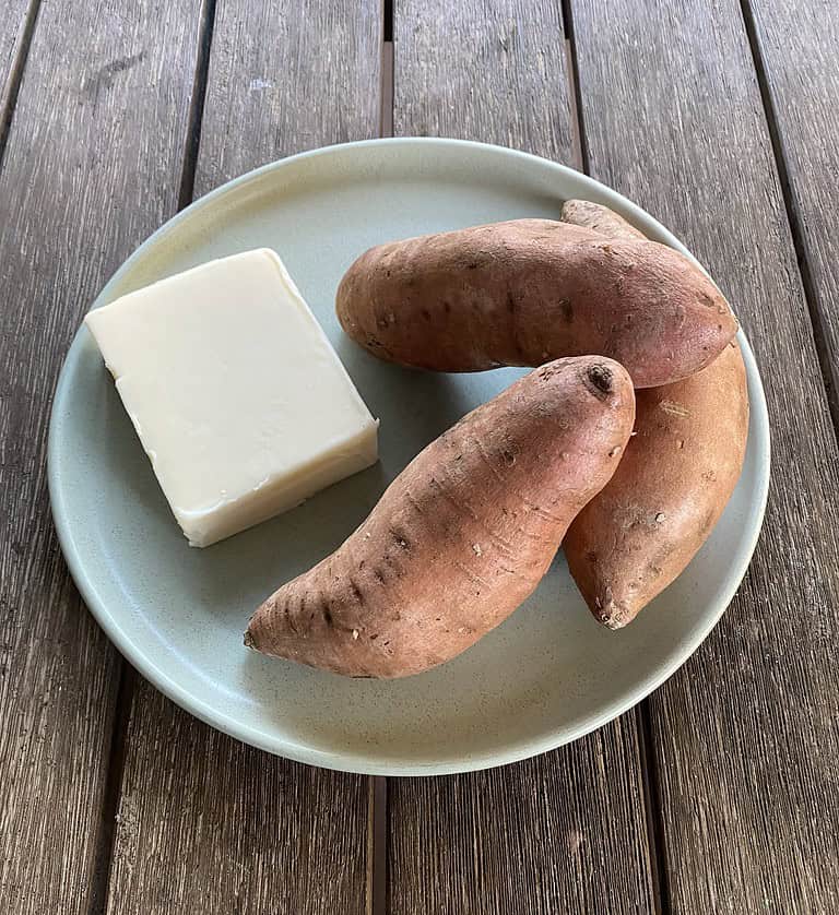 Sweet potatoes and a block of butterkäse cheese on a plate, ingredients used to analyze the nutritional value of the Butterkäse sweet potato recipe.